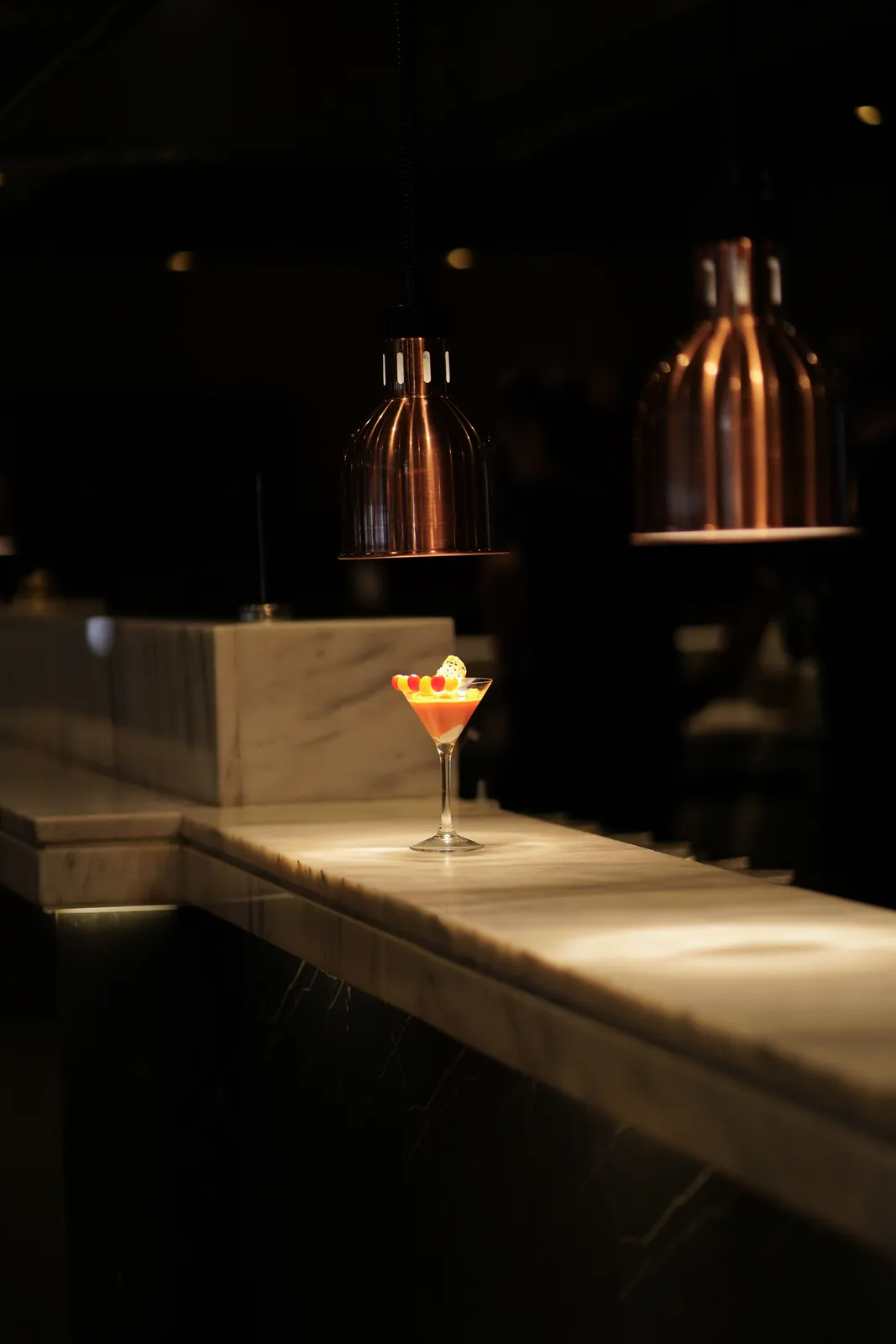 Signature cocktail πάνω στο μαρμάρινο μπαρ κάτω από χάλκινα φωτιστικά